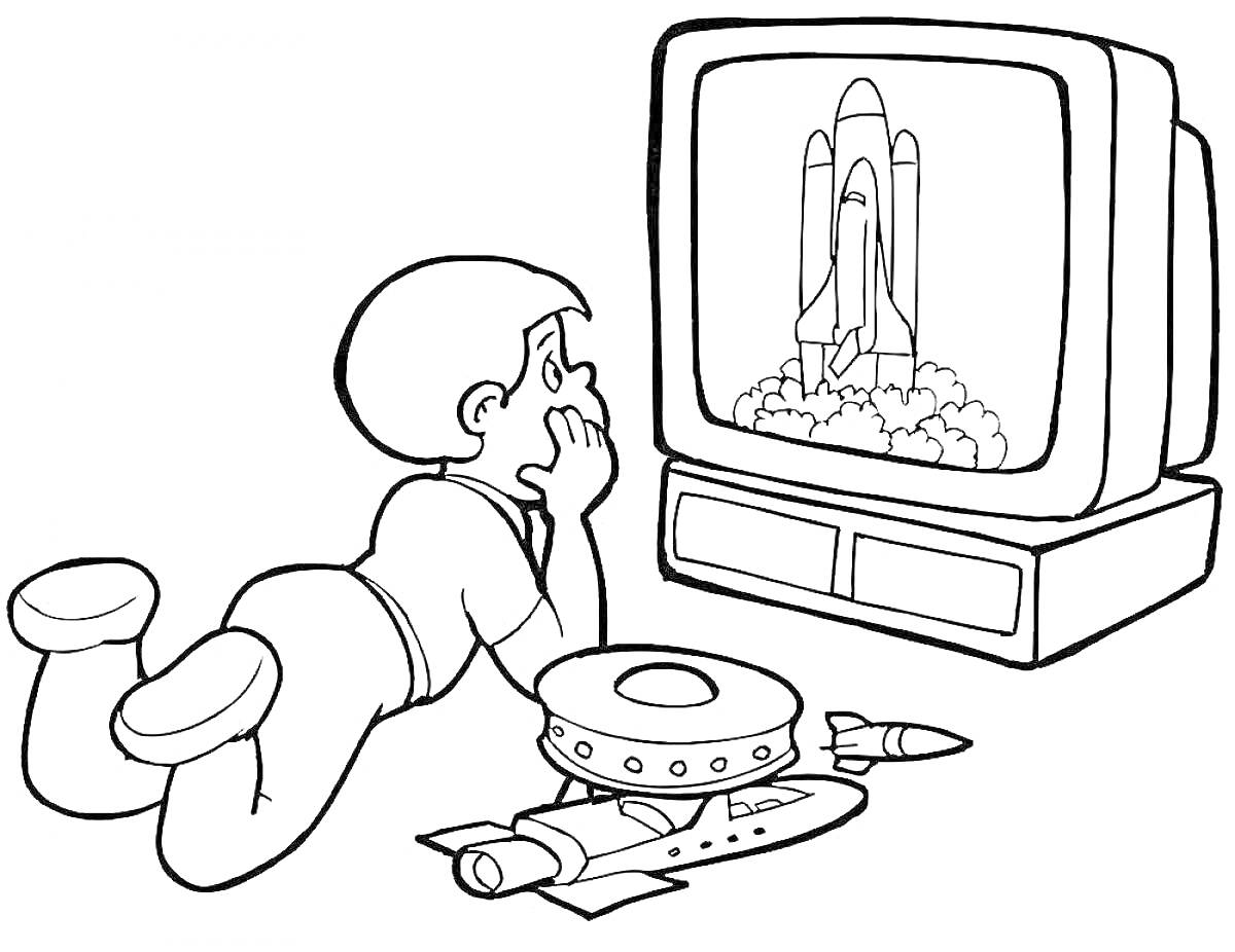 Мальчик смотрит телевизор с изображением ракеты, лежа на животе рядом с игрушечными ракетой и космическим кораблем